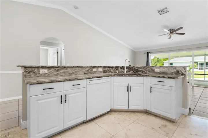 Kitchen with white dishwasher, a ceiling fan, dark stone counters, white cabinets, and arched walkways