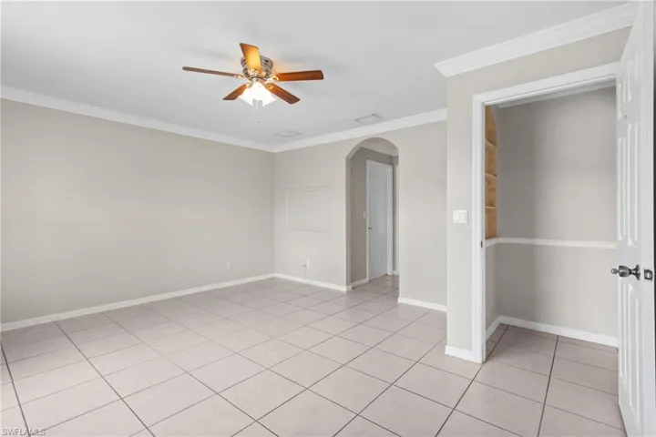 Spare room featuring a ceiling fan, arched walkways, crown molding, and light tile patterned floors