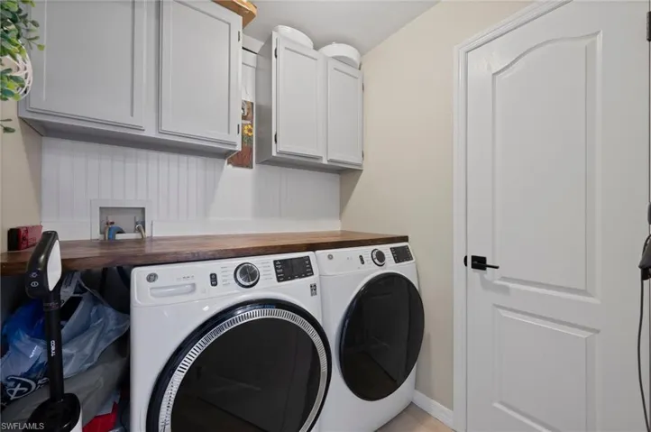 Laundry area featuring light gray cabinetry, a wood-finish countertop, white beadboard backsplash, and a white interior door with matte black hardware