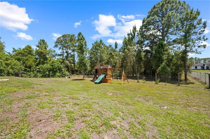Expansive grassy yard with a wooded perimeter, featuring a play structure with slide and swings, and partial fencing