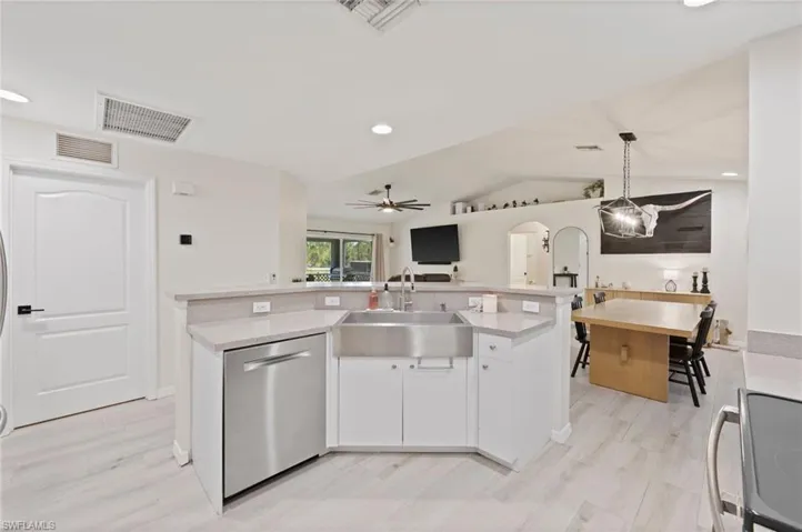 Modern kitchen featuring white cabinetry, light-toned countertops, a stainless steel farmhouse sink, and stainless steel dishwasher