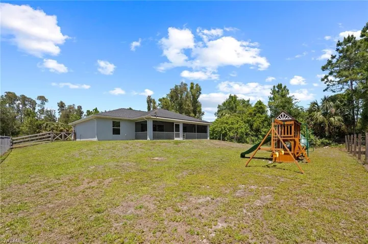 Expansive green space featuring a screened lanai, mature trees, and a privacy fence