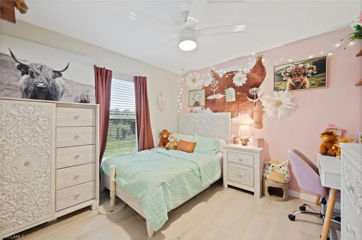 Bedroom featuring wood-finish flooring, a window with horizontal blinds and curtains, and a ceiling fan with integrated lighting