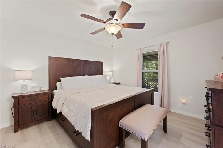 Spacious room featuring light-colored wood-finish flooring, a ceiling fan with integrated lighting, and a window with blinds and drapes