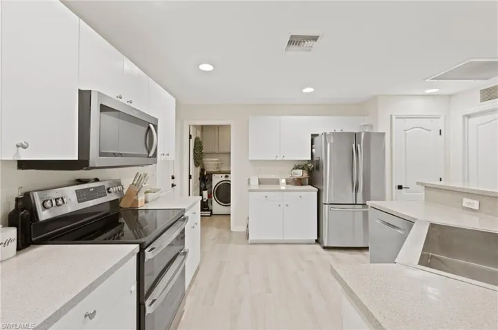 Modern kitchen featuring light wood-finish flooring, white cabinetry, and light-toned countertops