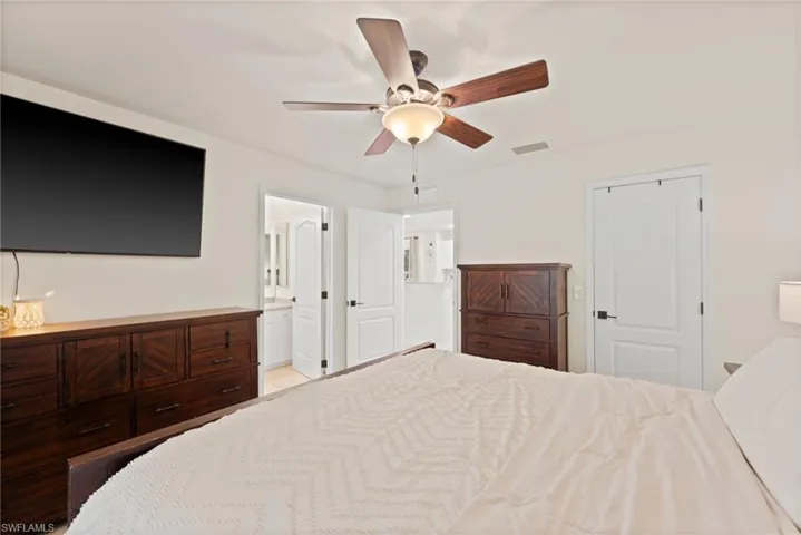 Bright bedroom featuring a ceiling fan with integrated lighting, white interior doors with dark hardware, and an open doorway revealing a bathroom with a white vanity