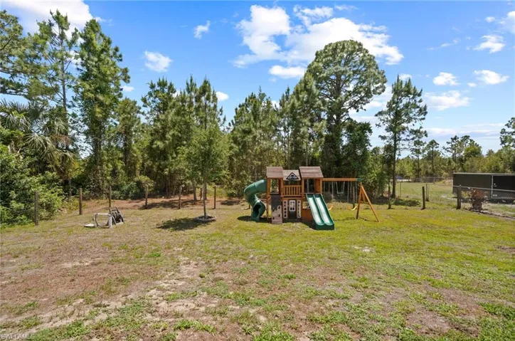 Expansive outdoor area featuring a wooden playset with two slides and a swing set, surrounded by mature trees and natural landscaping