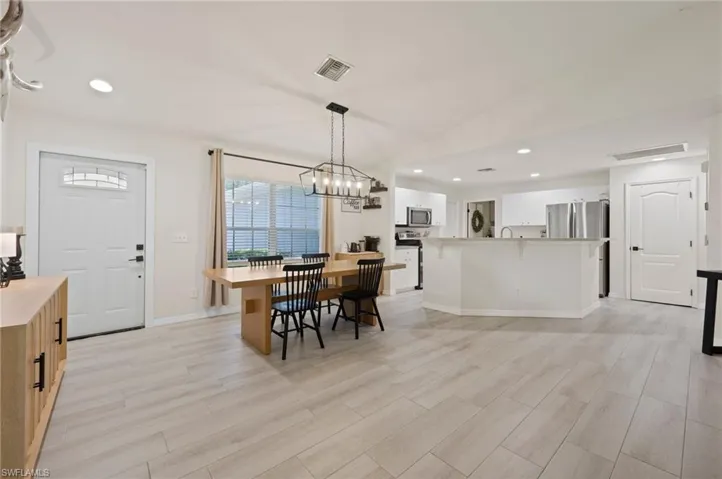 Open-concept living area featuring light wood-finish flooring, recessed lighting, a modern chandelier, and a kitchen island with a stone countertop