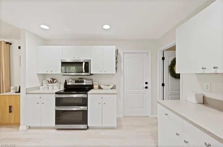 Bright kitchen featuring white cabinetry with silver hardware, recessed lighting, and light-tone countertops