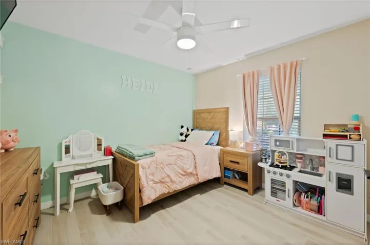 Bedroom featuring light wood-finish flooring, a ceiling fan with integrated lighting, and a window with horizontal blinds