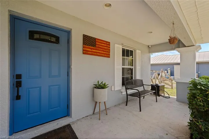 Covered entry porch featuring a blue panel door with an arched window, textured exterior walls, white window shutters, and concrete flooring