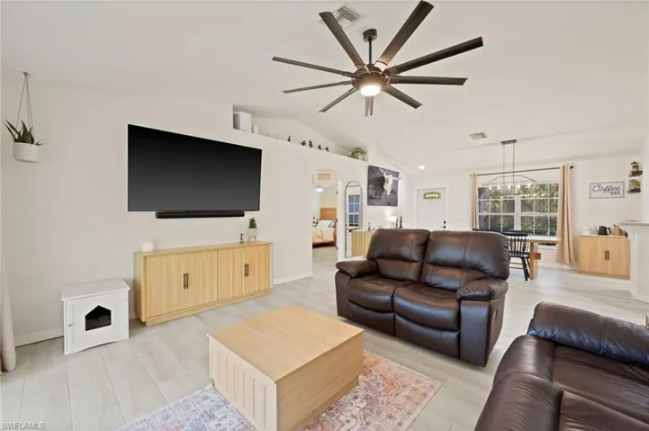 Spacious living area featuring light wood-finish flooring, a contemporary ceiling fan, vaulted ceilings, and a dedicated dining space with a modern linear chandelier