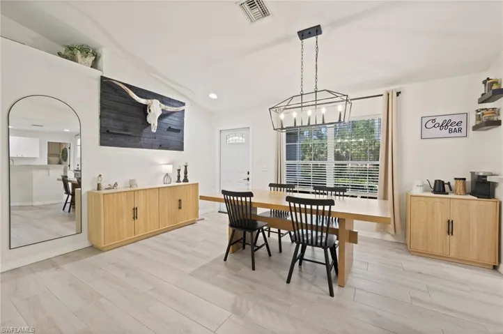 Spacious dining area featuring wood-finish flooring, a modern linear chandelier, an arched doorway, built-in shelving, and a large window with horizontal blinds