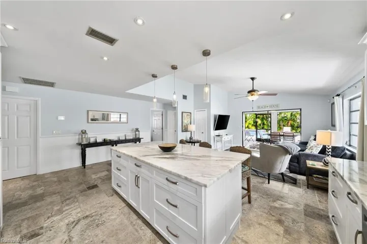 Kitchen featuring a kitchen bar, decorative light fixtures, light stone counters, white cabinetry, and vaulted ceiling