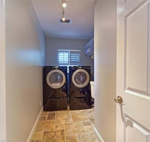 Laundry area with stone tile flooring, washing machine and dryer, and track lighting