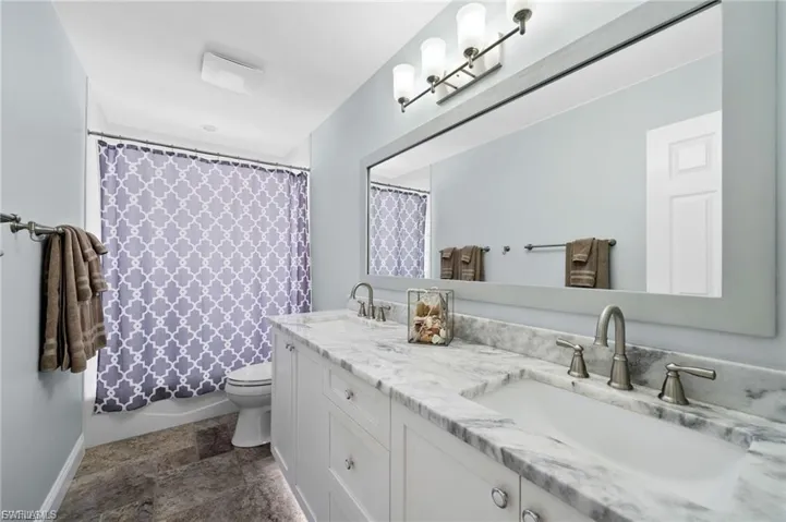 Full bath featuring double vanity, shower / tub combo, and stone finish flooring