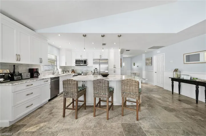 Kitchen featuring white cabinetry, a kitchen island, decorative light fixtures, a breakfast bar area, and lofted ceiling