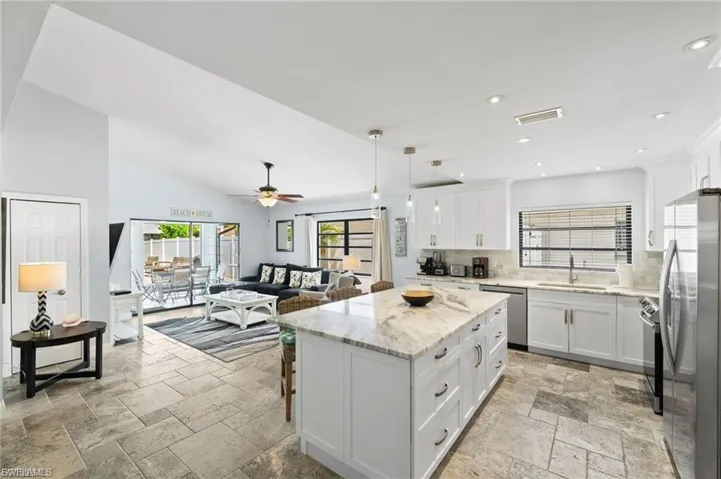 Kitchen featuring stone tile floors, decorative backsplash, open floor plan, a center island, and high vaulted ceiling