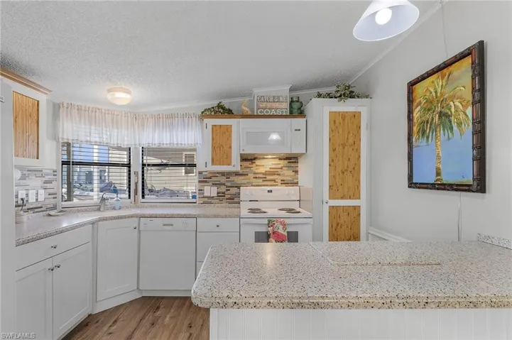Kitchen featuring white appliances, white cabinets, light hardwood / wood-style flooring, vaulted ceiling, and ornamental molding
