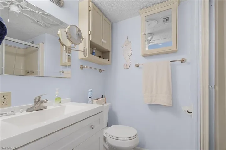 Bathroom with vanity, a textured ceiling, toilet, and a shower with door
