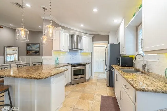 Kitchen featuring appliances with stainless steel finishes, white cabinets, sink, decorative backsplash, and wall chimney exhaust hood
