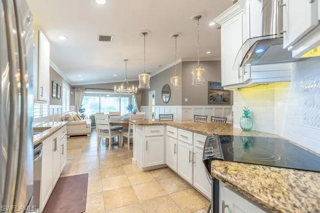 Kitchen featuring appliances with stainless steel finishes, decorative backsplash, light stone countertops, and white cabinetry
