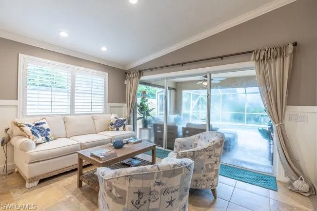 Living room with lofted ceiling, crown molding, light tile patterned floors, and ceiling fan