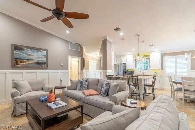 Living room featuring light tile patterned flooring, crown molding, ceiling fan with notable chandelier, and vaulted ceiling