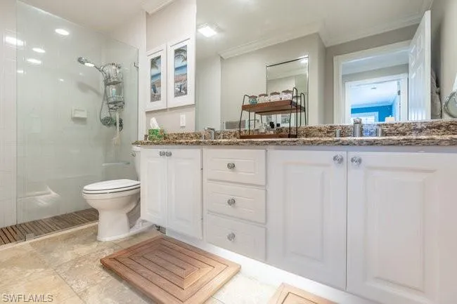 Bathroom with a tile shower, tile patterned floors, toilet, ornamental molding, and double sink vanity
