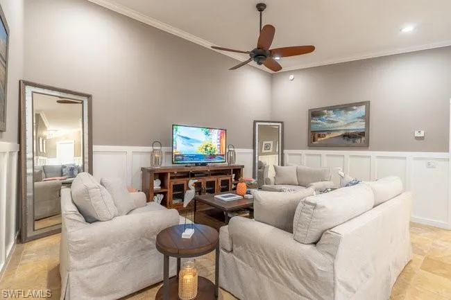 Living room with a towering ceiling, crown molding, light tile patterned floors, and ceiling fan