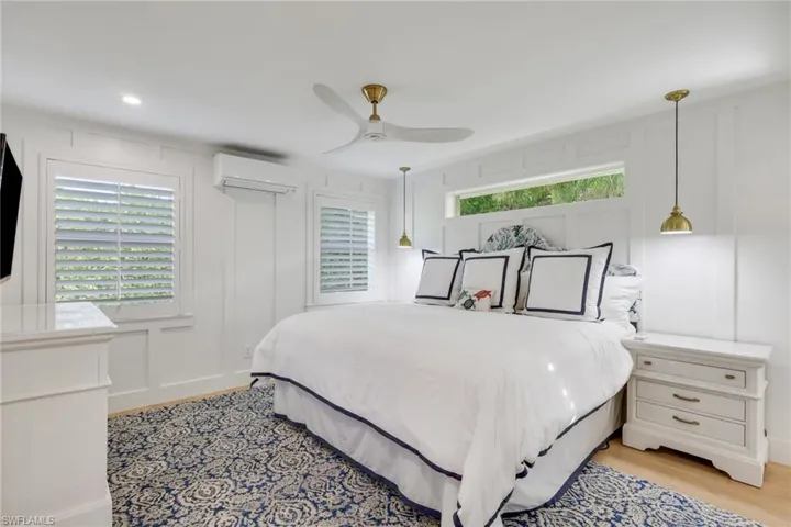 Bedroom featuring a decorative wall, ceiling fan, multiple windows, a wall mounted AC, and light wood-style floors