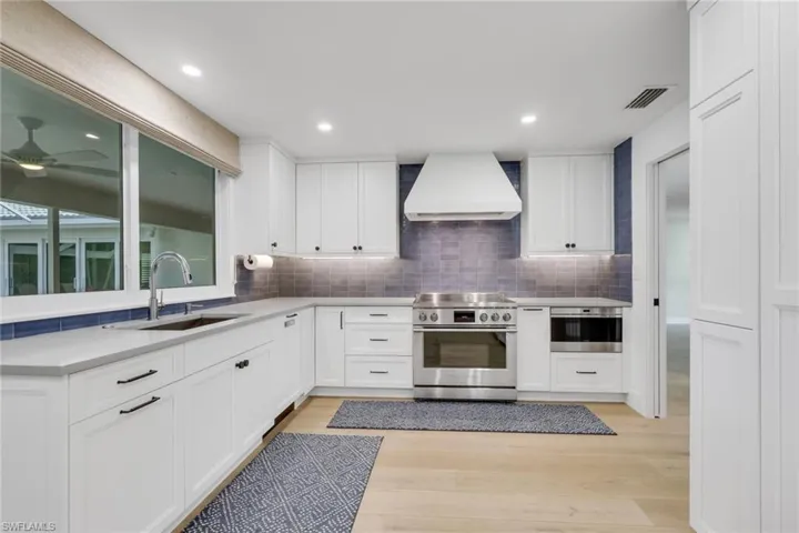 Kitchen featuring white cabinets, custom range hood, stainless steel appliances, and light wood-style floors