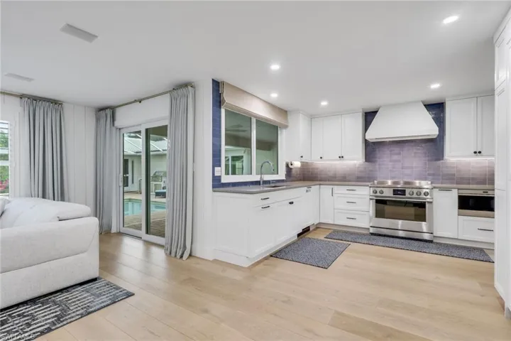 Kitchen featuring white cabinets, stainless steel appliances, custom exhaust hood, and light wood finished floors