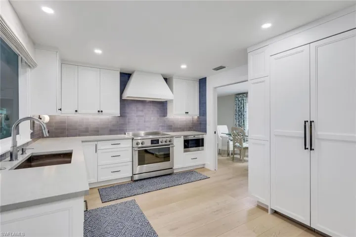 Kitchen featuring stainless steel appliances, white cabinets, custom exhaust hood, light wood finished floors, and tasteful backsplash
