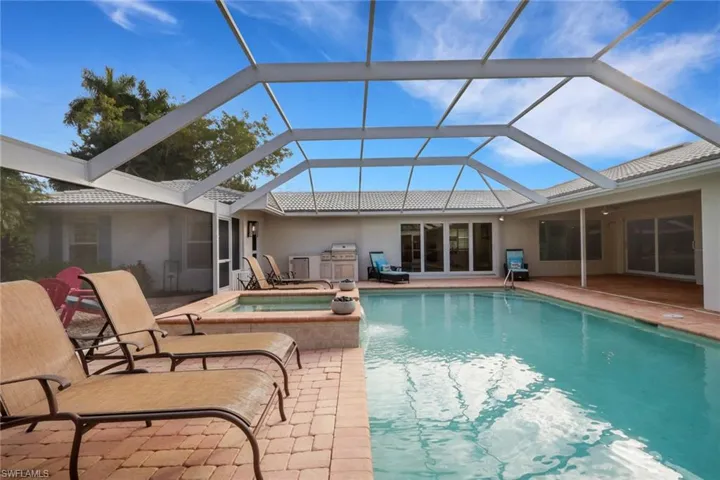 View of pool featuring a sunroom, a pool with connected hot tub, grilling area, and glass enclosure