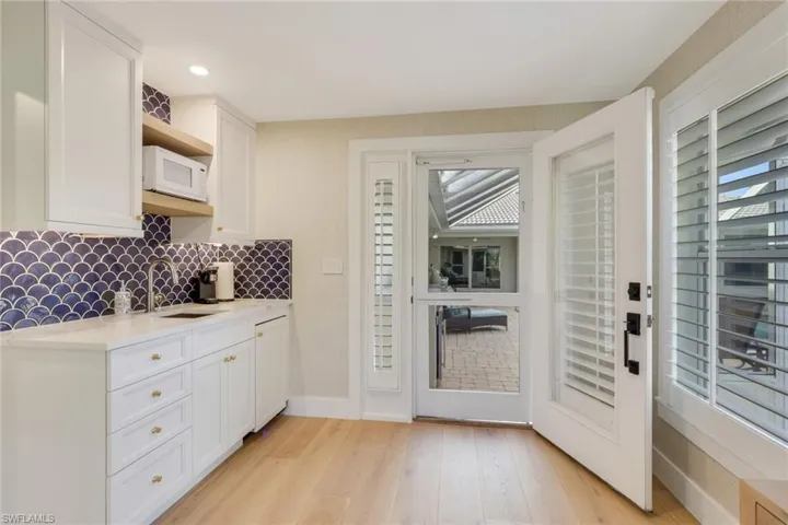 Kitchen with white cabinets, light stone countertops, white microwave, tasteful backsplash, and light wood-type flooring
