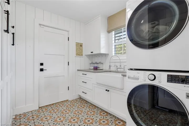 Washroom with stacked washing machine and dryer, cabinet space, and light tile patterned floors