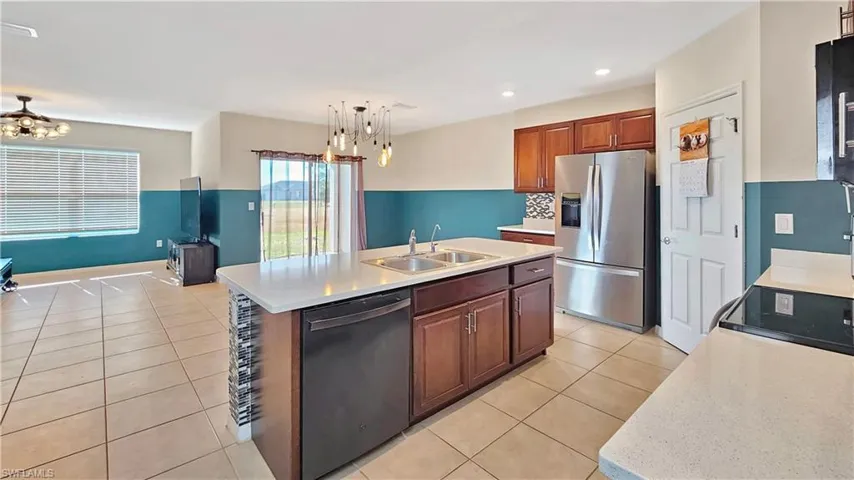 Kitchen featuring appliances with stainless steel finishes, sink, a center island with sink, decorative light fixtures, and light tile patterned flooring