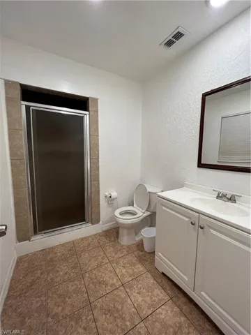 Bathroom featuring a textured wall, vanity, a stall shower, and light tile patterned flooring