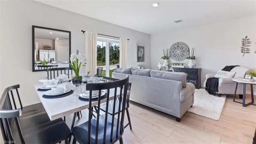 The open concept living area features light-toned flooring, a dining space with a rectangular table, and a living room with a sliding glass door providing a view of the outdoors