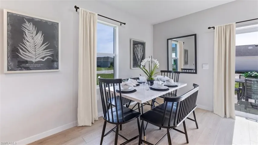 This dining area features light-colored flooring, a window with a curtain, and a glass sliding door providing access to an outdoor patio