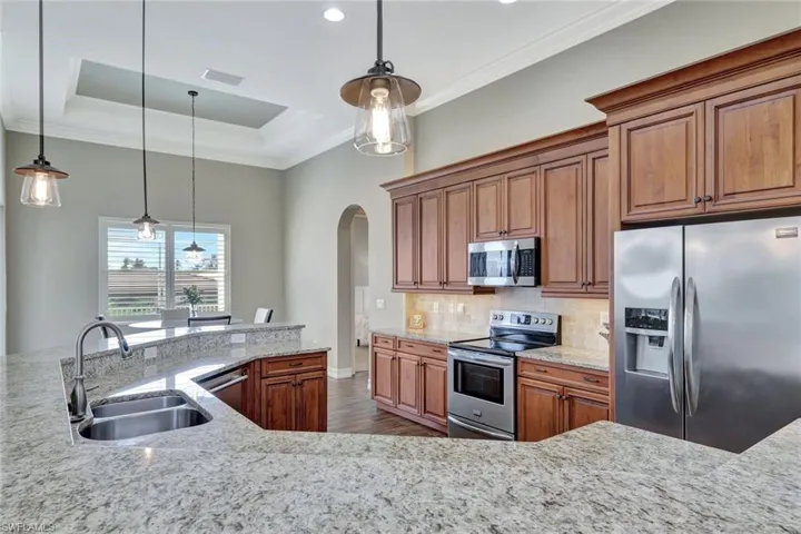 Kitchen featuring stainless steel appliances, a sink, hanging light fixtures, and light stone counters