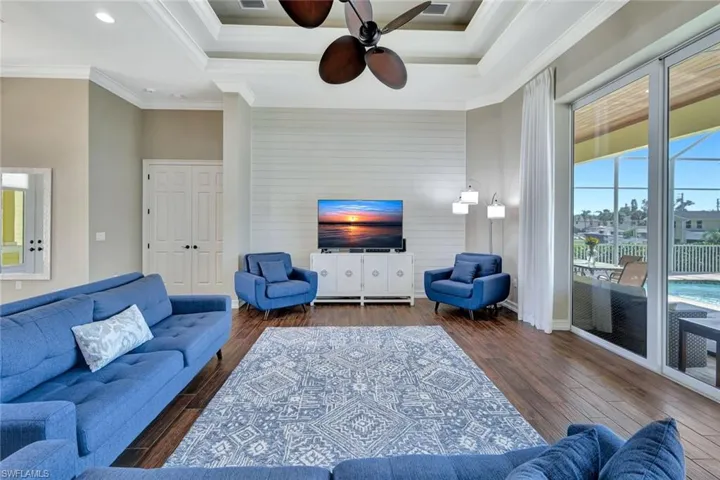 Living room featuring a tray ceiling, visible vents, ornamental molding, and dark wood-style flooring