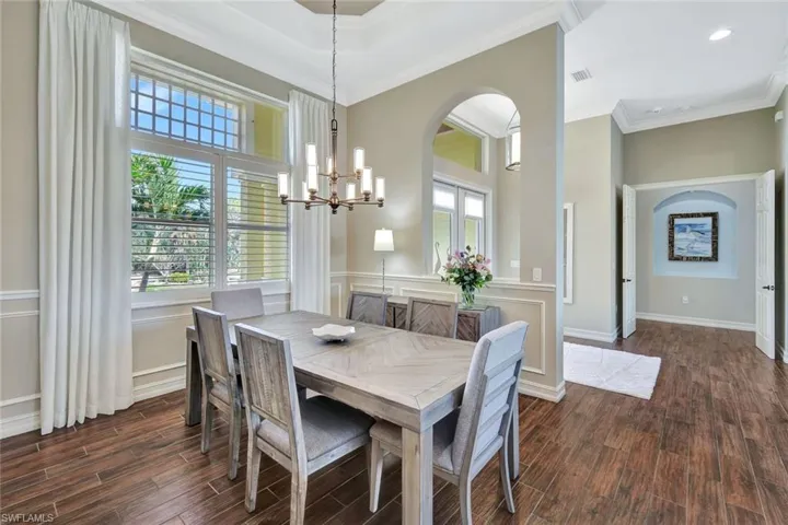 Dining area featuring an inviting chandelier, ornamental molding, arched walkways, and dark wood-style flooring
