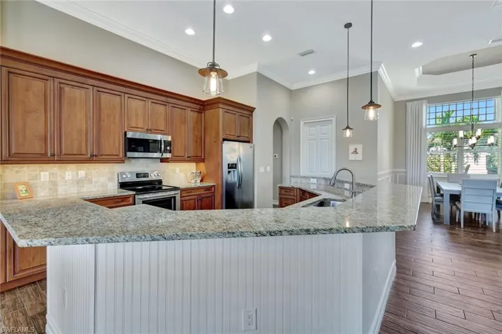 Kitchen with arched walkways, brown cabinetry, appliances with stainless steel finishes, hanging light fixtures, and a sink