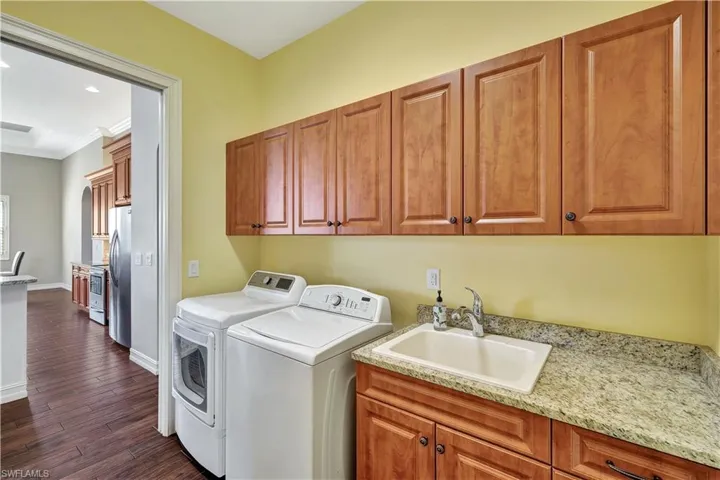 Clothes washing area with washing machine and clothes dryer, cabinet space, dark wood-type flooring, a sink, and baseboards