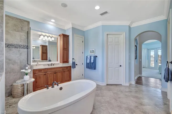 Bathroom featuring baseboards, visible vents, vanity, a freestanding bath, and crown molding