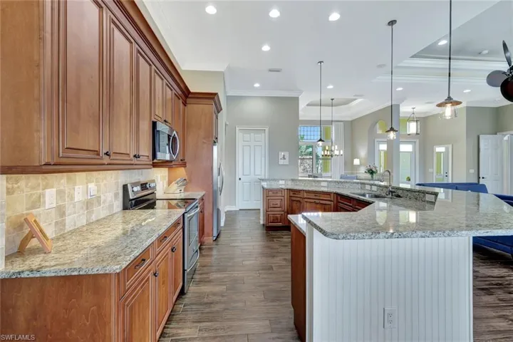 Kitchen featuring stainless steel appliances, a sink, brown cabinets, dark wood finished floors, and decorative light fixtures
