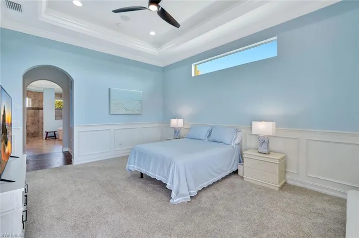 Bedroom with arched walkways, visible vents, light carpet, and a tray ceiling