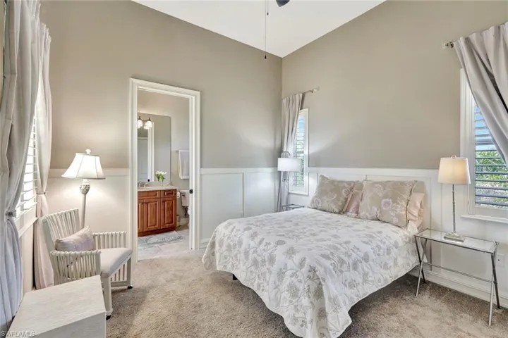 Bedroom with radiator, a wainscoted wall, ensuite bath, and light colored carpet
